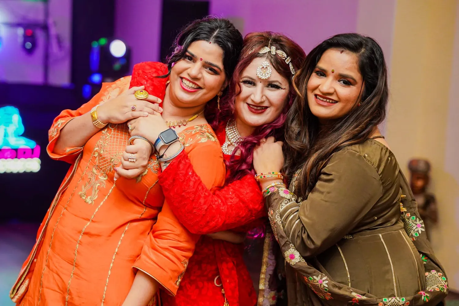 Three women in festive clothes hugging and smiling